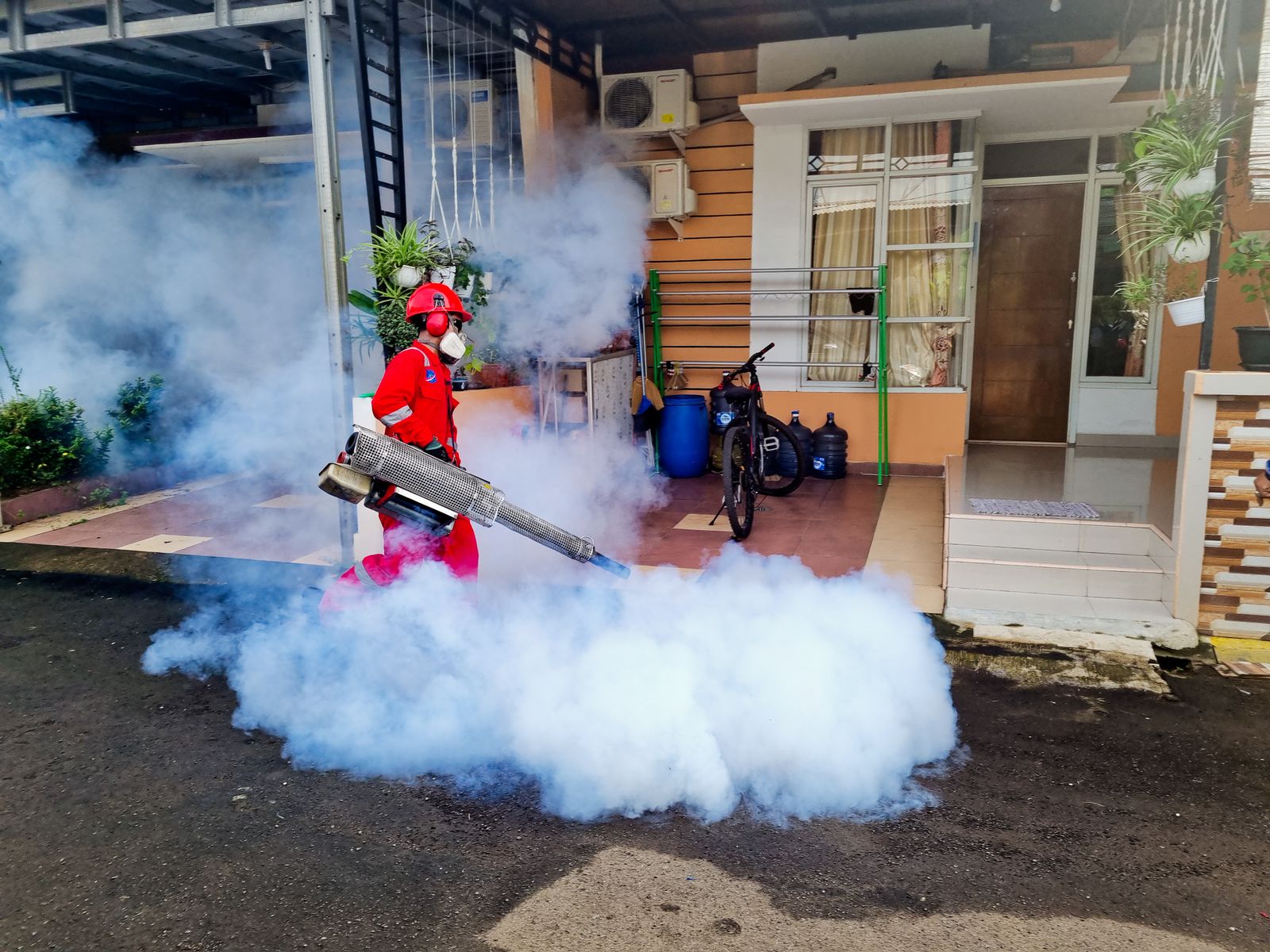 A Summit Pest Control technician in protective gear fogging the exterior perimeter of a home